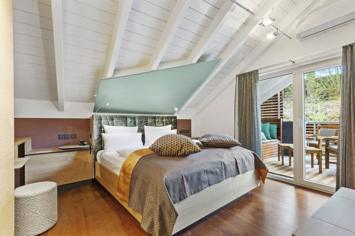 A modern bedroom with a large bed, a desk, and a sliding glass door leading to an outdoor area.