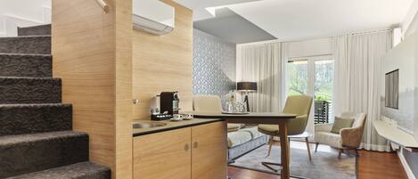 Una cocina moderna con una escalera de madera, una zona de comedor con mesa y sillas, y una sala de estar con sofá y televisor.