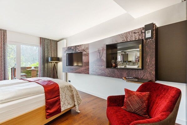 Une chambre d’hôtel moderne avec un grand lit, un fauteuil rouge, un téléviseur fixé au mur et une grande fenêtre avec des rideaux.
