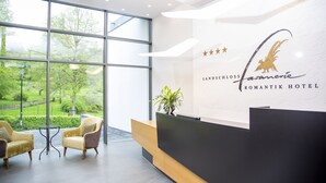 A reception desk with a view of a garden, a logo for 'Romantik Hotel', and a sign indicating 'Landschloss'. - Romantik Hotel Landschloss Fasanerie (Zweibruecken)