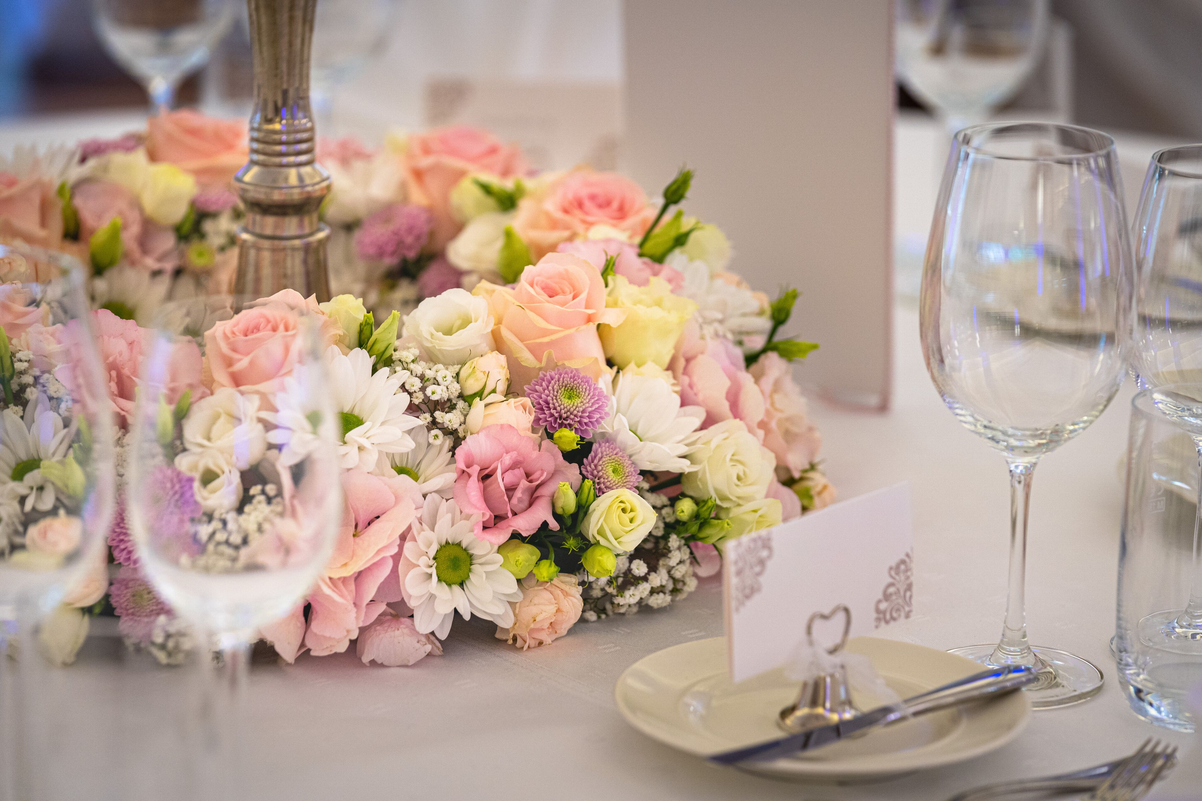 Una mesa dispuesta con un centro de mesa floral, copas de vino y un plato con un tenedor.