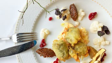 Een bord eten met diverse ingrediënten, waaronder gefrituurde stukken, kaas en gedroogd fruit, met een vork en mes op een wit bord met een gouden rand.