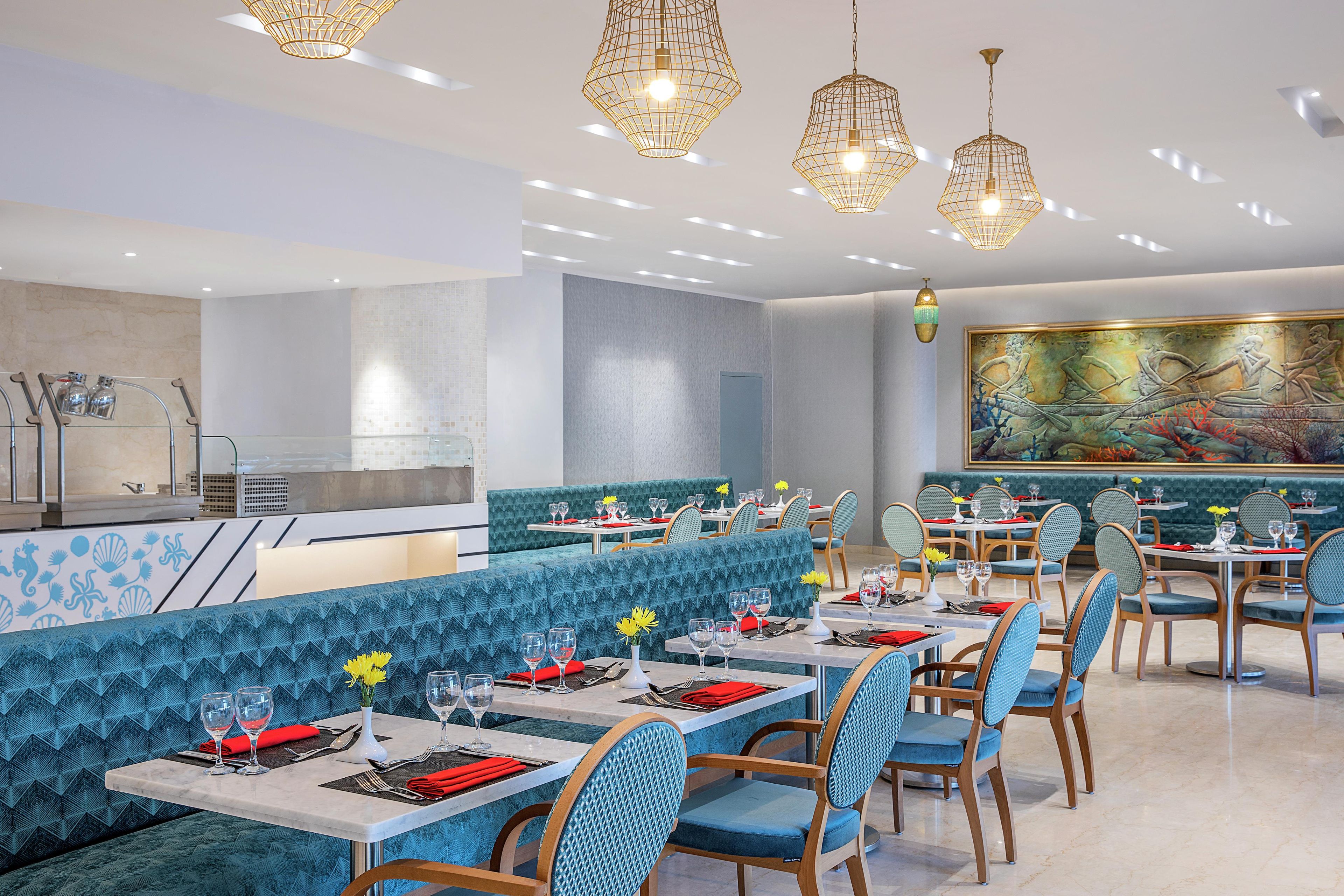 Un restaurante con asientos tapizados en azul, sillas de madera y un gran mural en la pared.