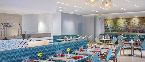 Un restaurante con asientos tapizados en azul, sillas de madera y un gran mural en la pared.