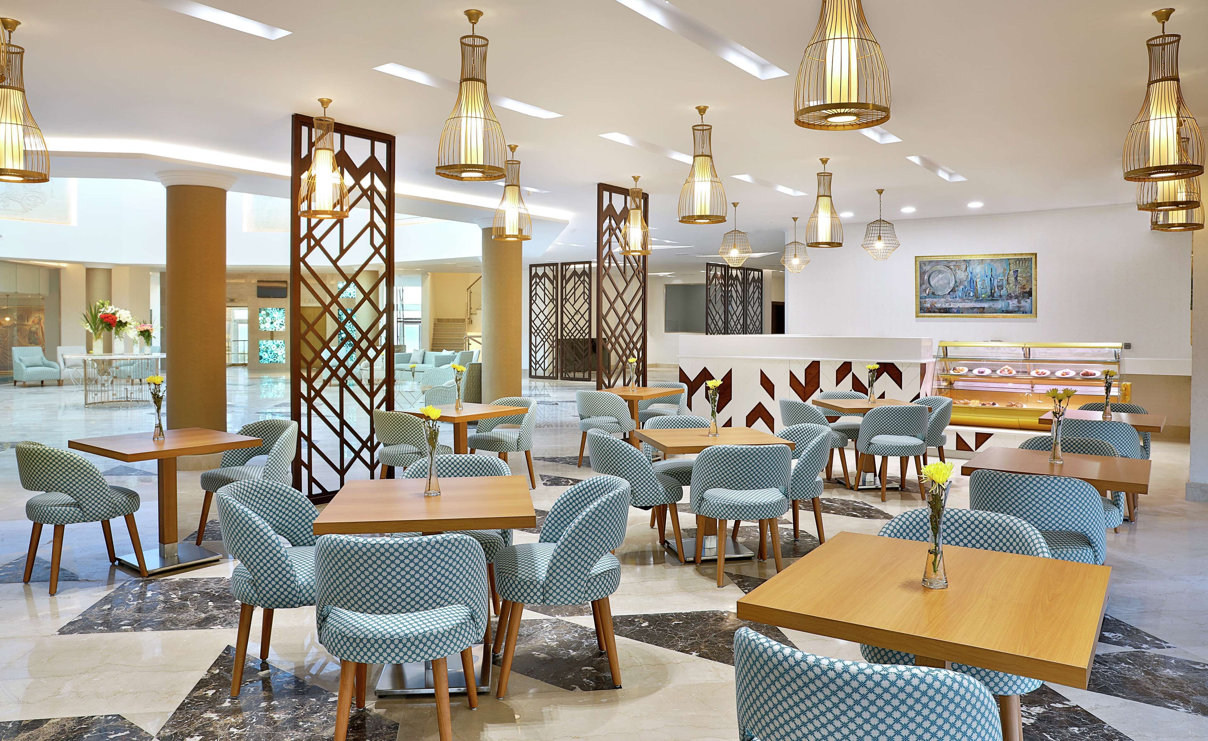A spacious hotel lobby with multiple seating areas, including tables and chairs, and a food display counter.
