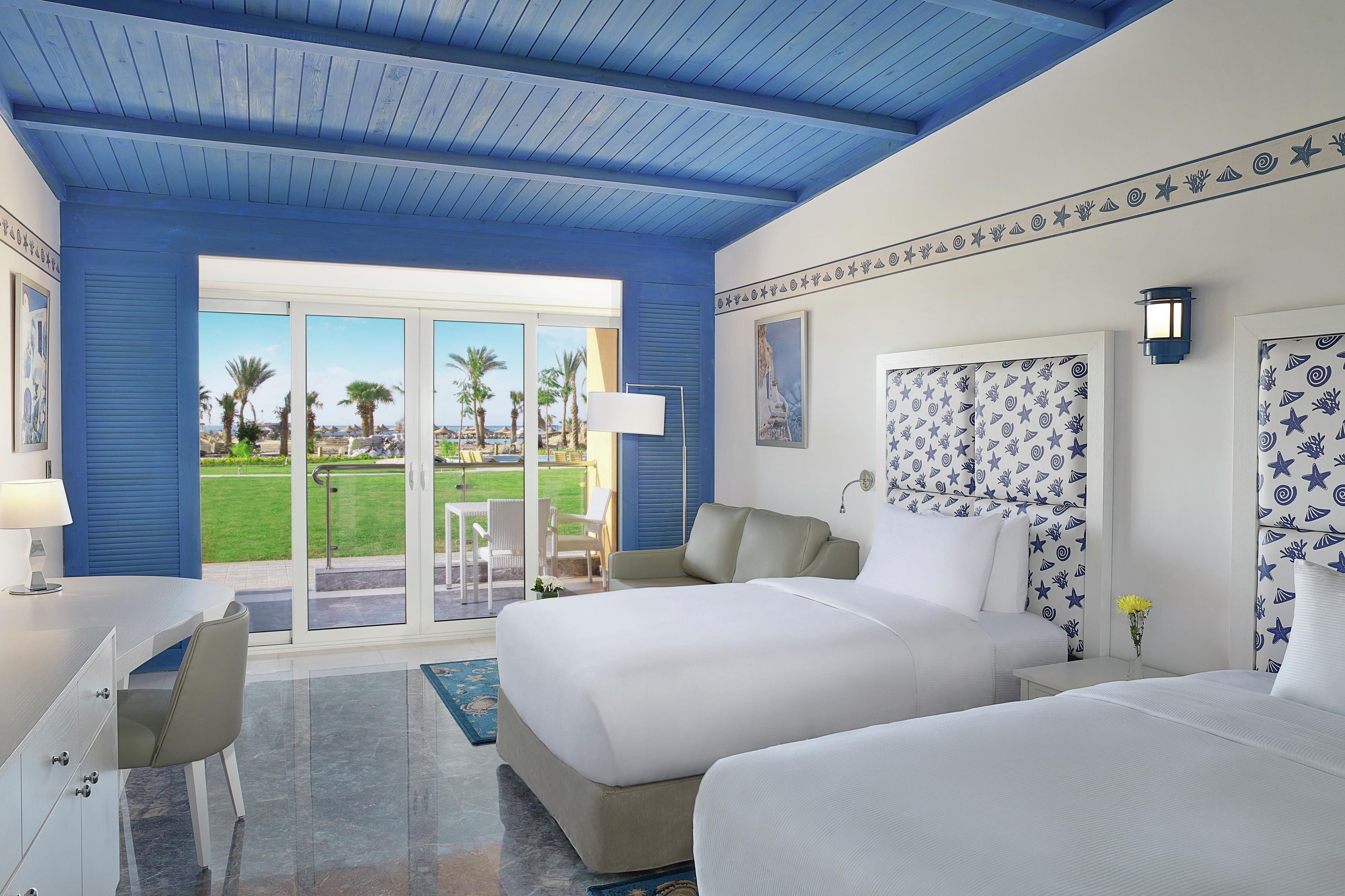 A hotel room with a large bed, a desk, and a view of a pool and palm trees.
