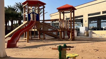 Ein Spielplatz mit Rutsche und Klettergerüsten vor einem Gebäude mit großen Fenstern.