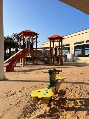 A playground with a slide and climbing structures, set against a building with large windows. - Hilton Hurghada Plaza (Hurghada)