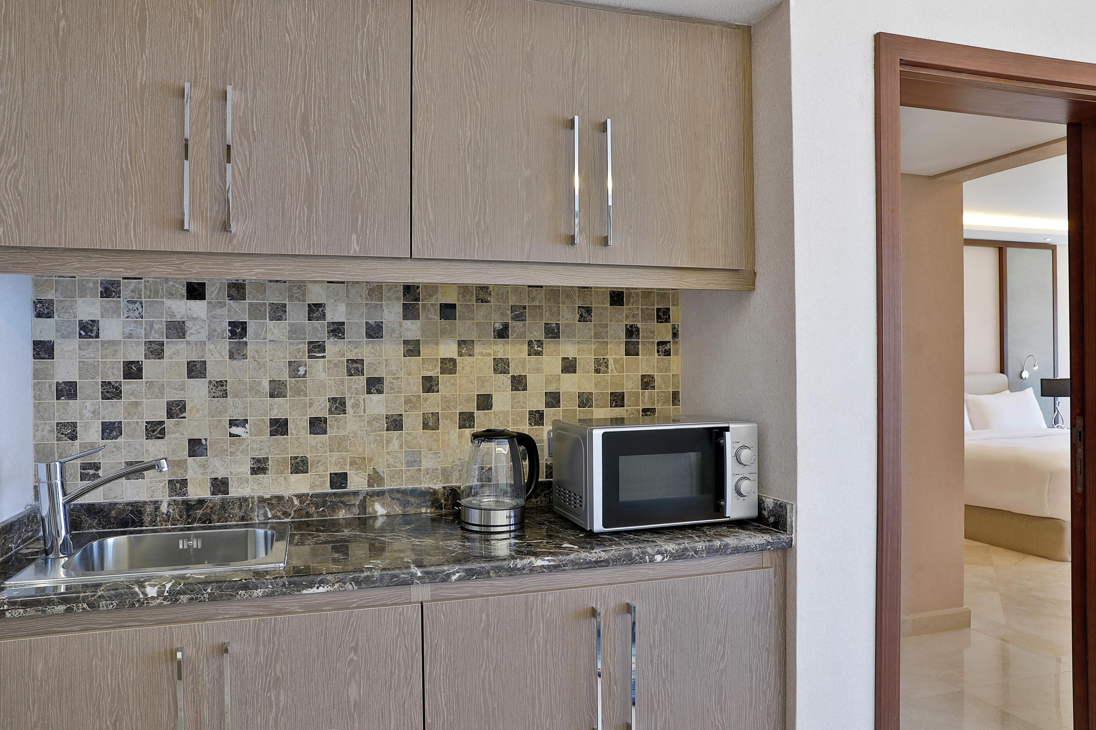 A compact kitchen with a microwave, kettle, and stainless steel sink.