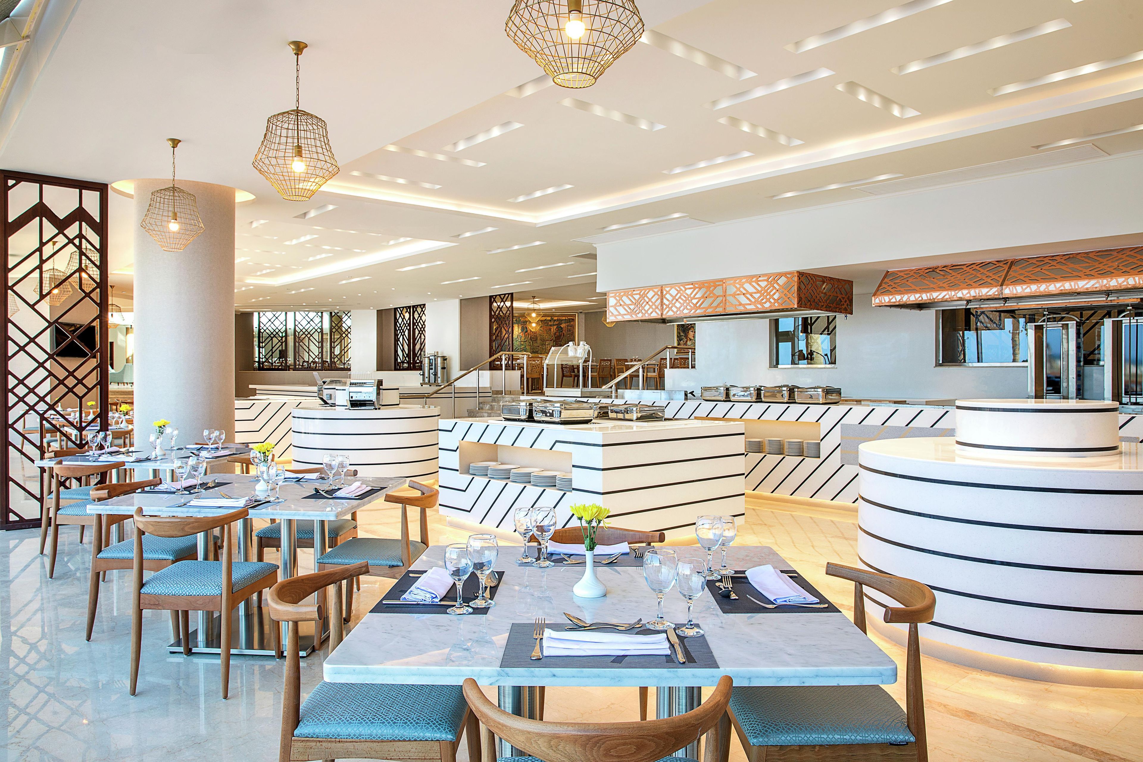 Un interno ristorante moderno con soffitti alti, motivi geometrici a soffitto e lampade dal design contemporaneo.