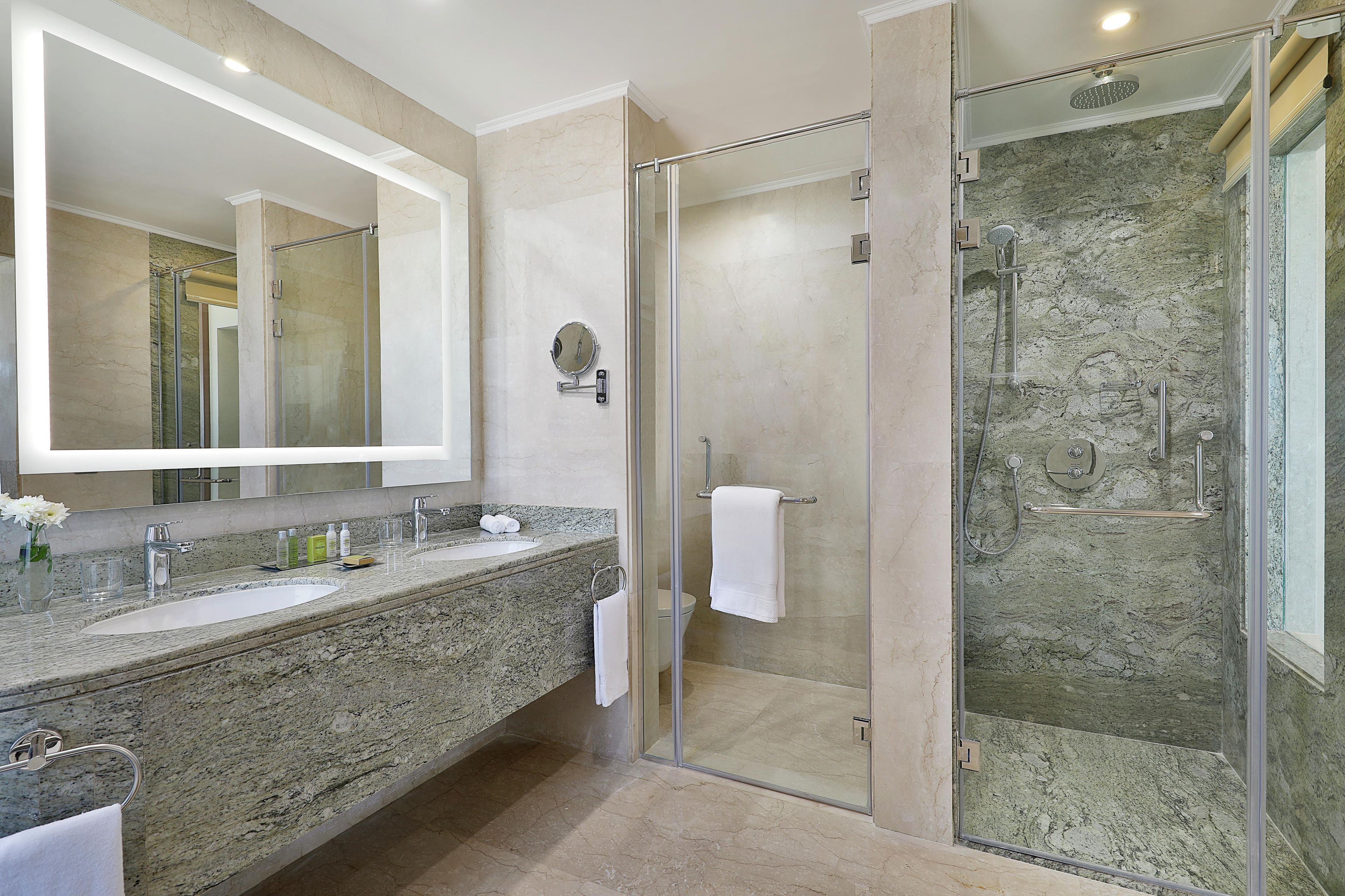 A bathroom with a large mirror, two sinks, a glass-enclosed shower, and a marble countertop.