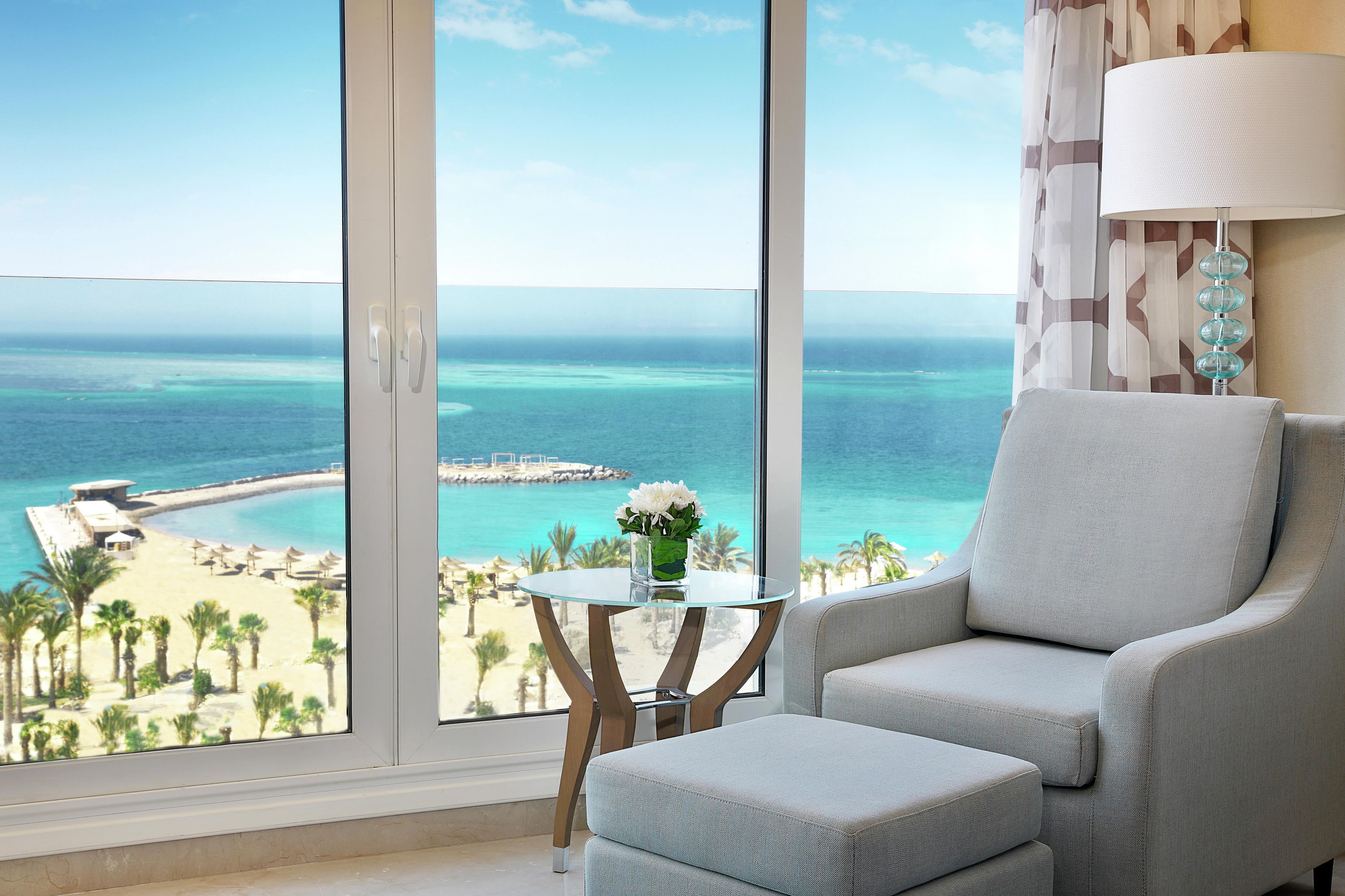 A room with a large window offering a view of a beach and ocean.