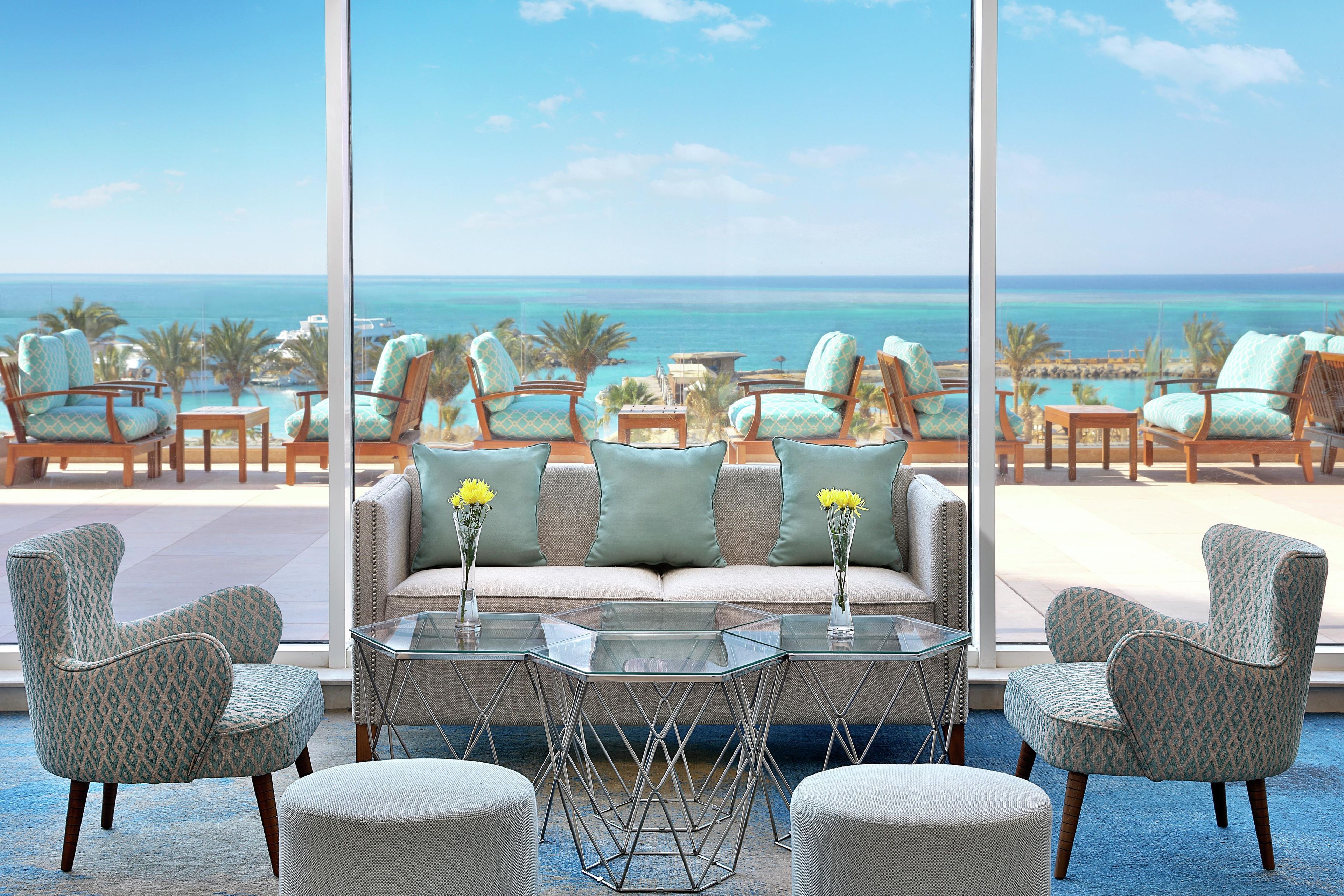 Un espace détente avec un canapé, des fauteuils et une table basse, offrant une vue sur la plage et l’océan.