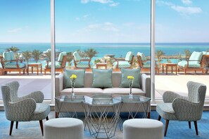 A lounge area with a sofa, armchairs, and a coffee table, overlooking a beach and ocean view. - Hilton Hurghada Plaza (Hurghada)