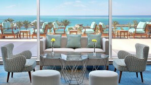 A room with a large window overlooking the ocean, furnished with a sofa, armchairs, and a glass coffee table. - Hilton Hurghada Plaza (Hurghada)