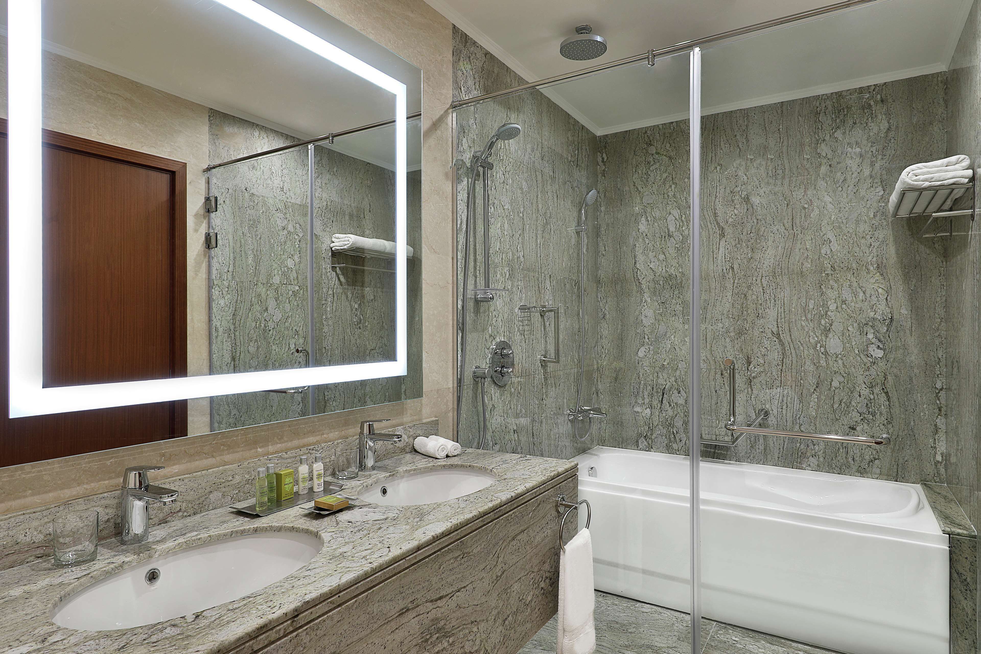 A modern bathroom with a large mirror, two sinks, a bathtub, and a glass-enclosed shower.
