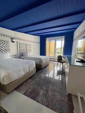 Habitación de hotel con dos camas, un escritorio y un ventanal grande.