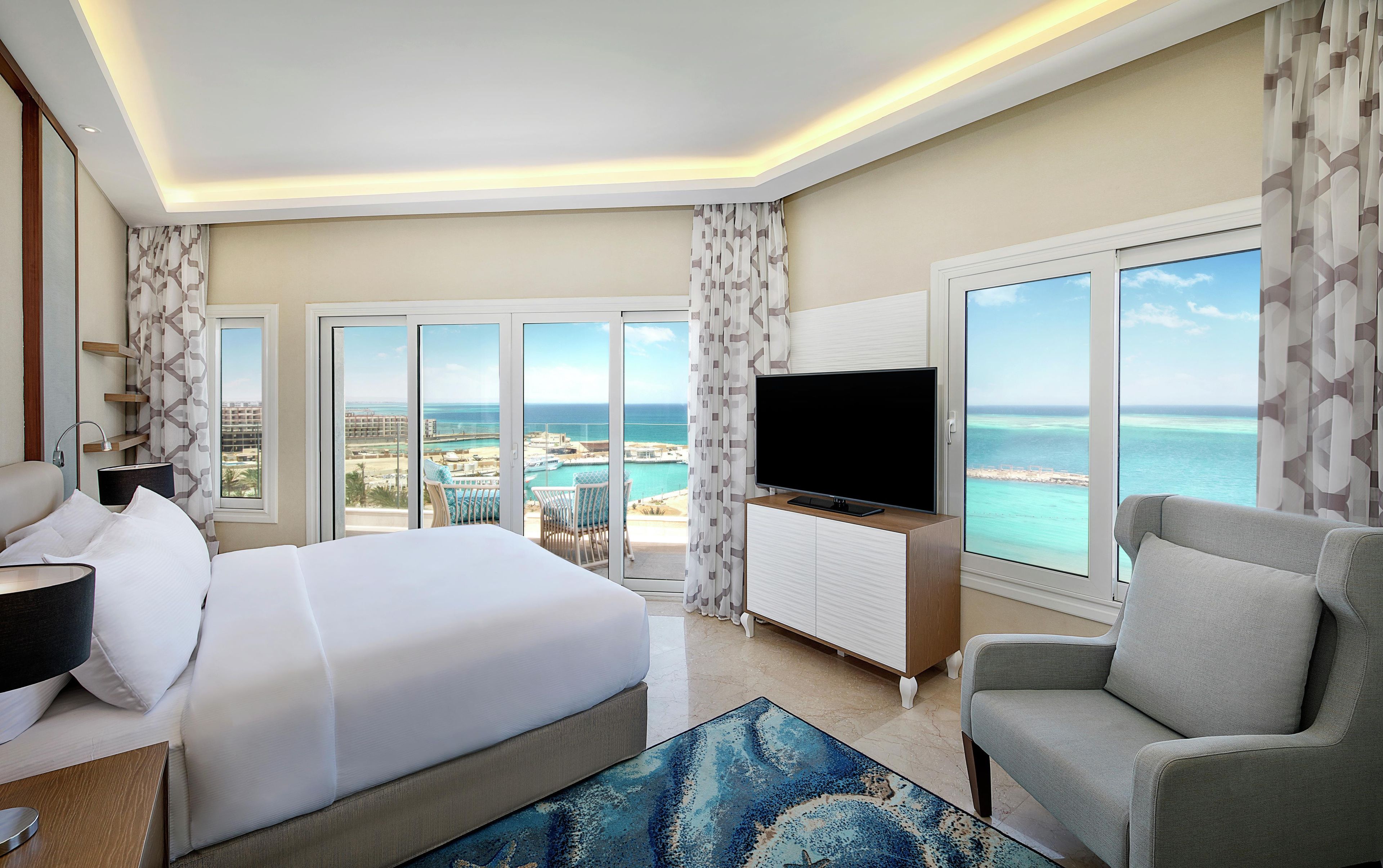 Een hotelkamer met een bed, een televisie, een zithoek en uitzicht op de oceaan.