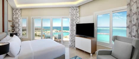 Una habitación de hotel con una cama, televisor, zona de estar y vistas al océano.
