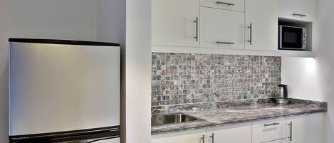 Una cocina moderna con armarios blancos, un refrigerador de acero inoxidable, salpicadero de azulejos y un microondas.