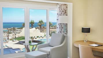 A room with a view of the beach, a chair, a small table, and a lamp.