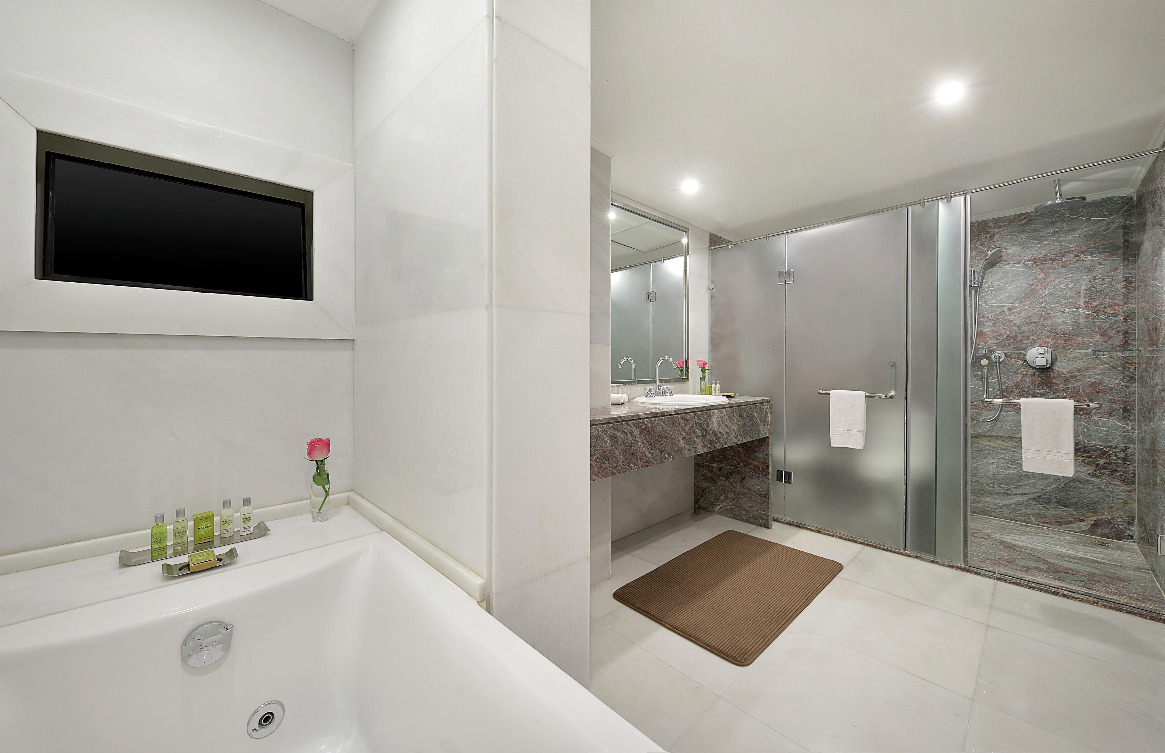 Un baño con bañera, ducha con puerta de vidrio, tocador con espejo y artículos de aseo.