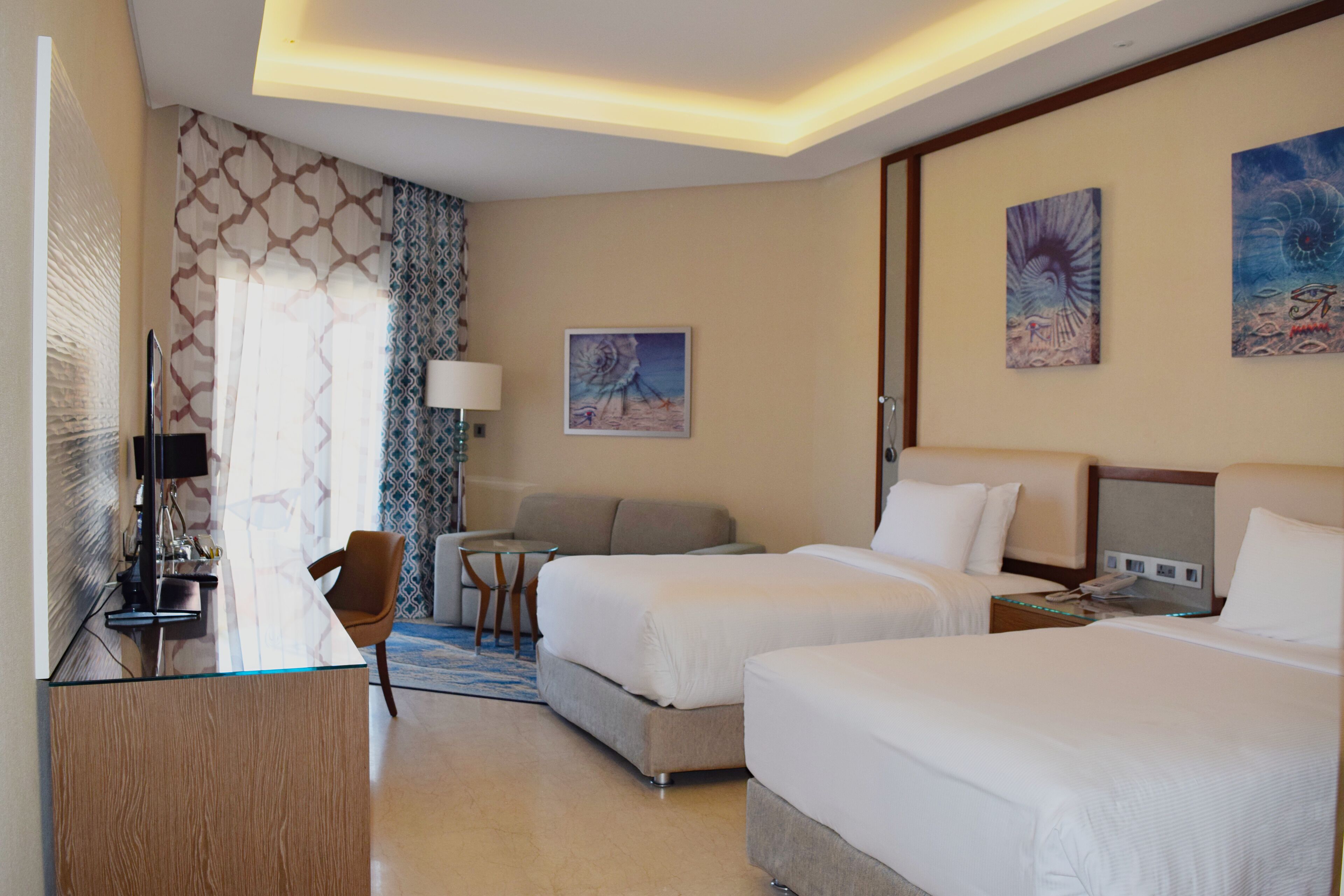 Una habitación de hotel con dos camas, un escritorio, un televisor y obras de arte en las paredes.