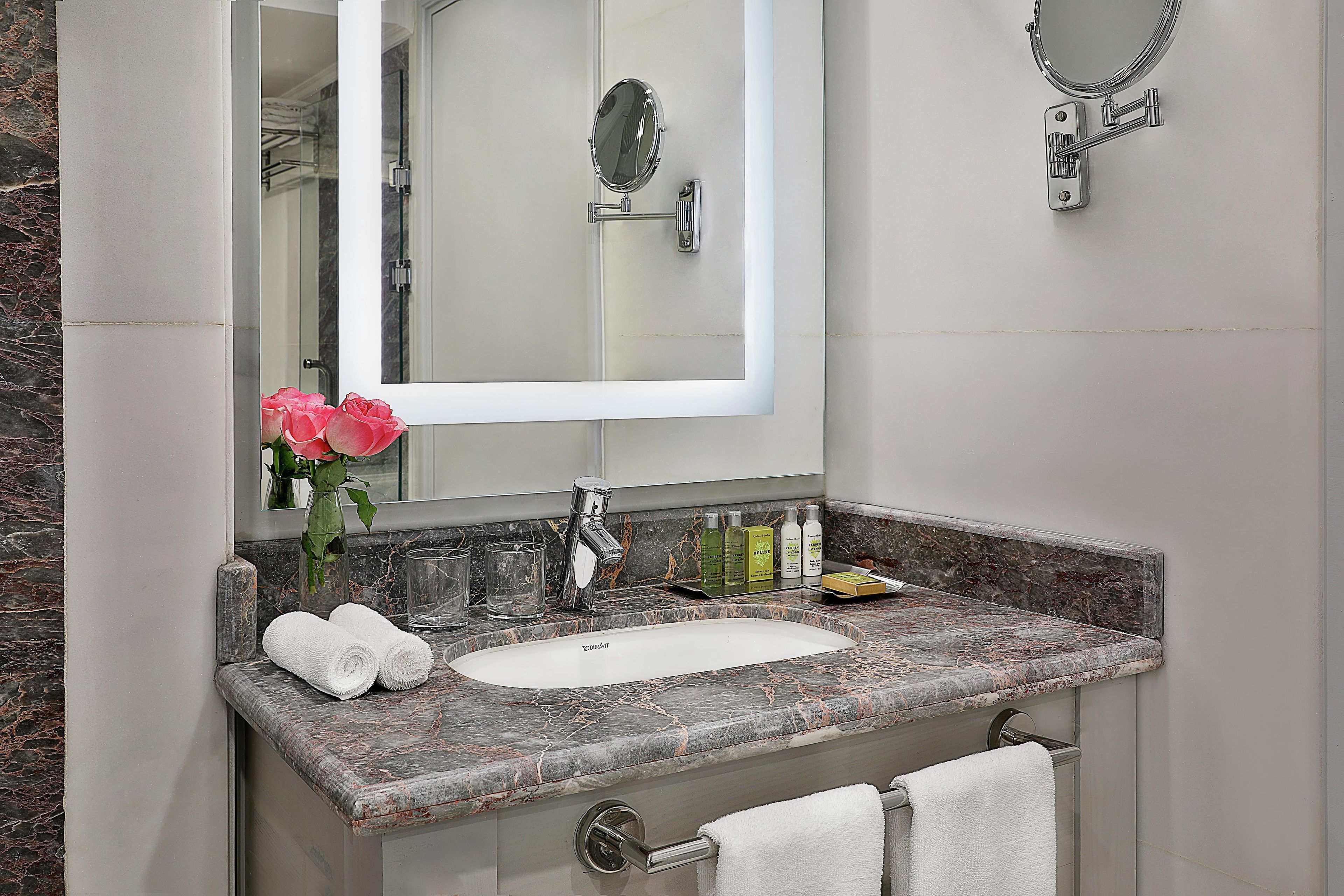 Un bagno con un lavabo in marmo, un lavandino, uno specchio, un portasciugamani e un vaso con fiori.