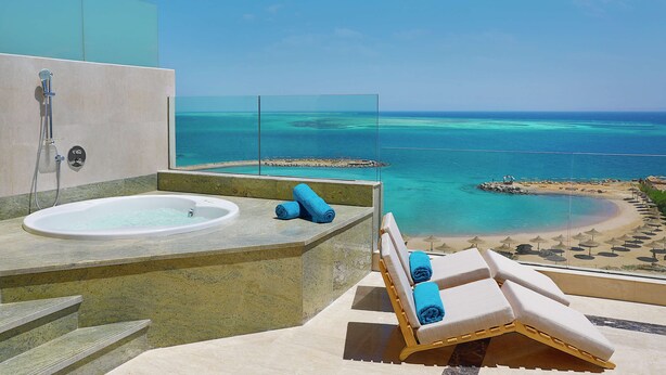 A balcony with a bathtub, lounge chairs, and a view of a beach and ocean. - Hilton Hurghada Plaza (Hurghada)