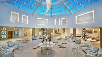 A spacious lobby with a high ceiling and skylight, featuring seating areas and artwork on the walls.