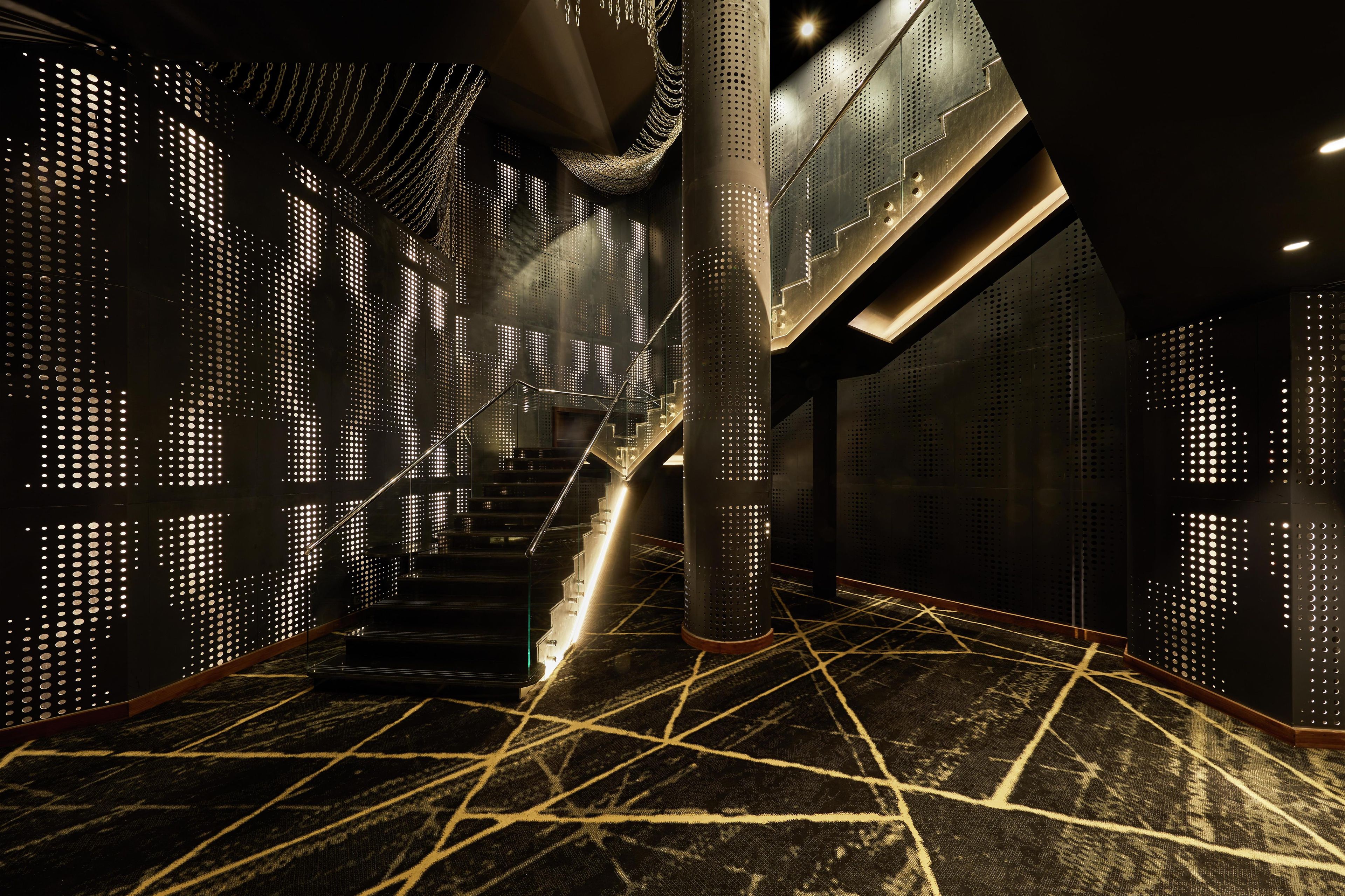 Un intérieur moderne avec un motif géométrique au sol, un escalier central et des murs perforés.