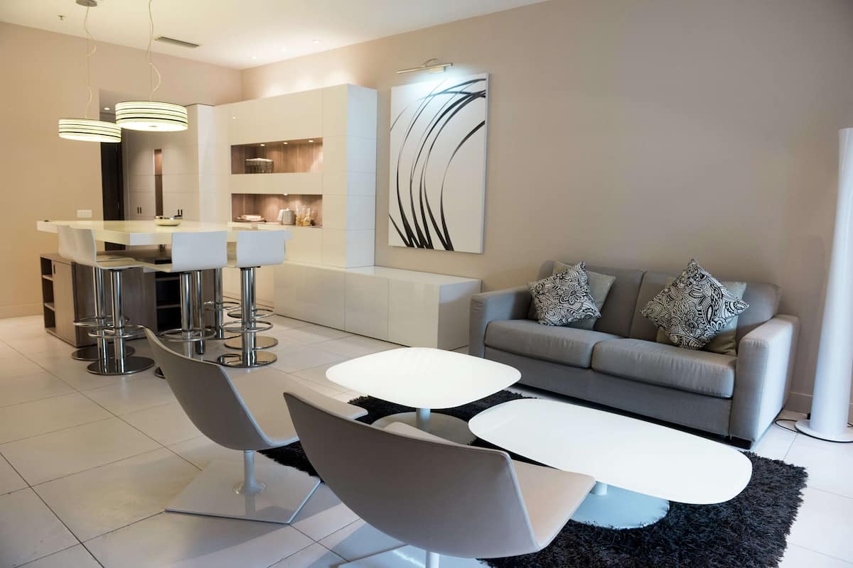 Un salon moderne avec un canapé gris, deux tables basses blanches et un coin repas comprenant une table et des chaises blanches.