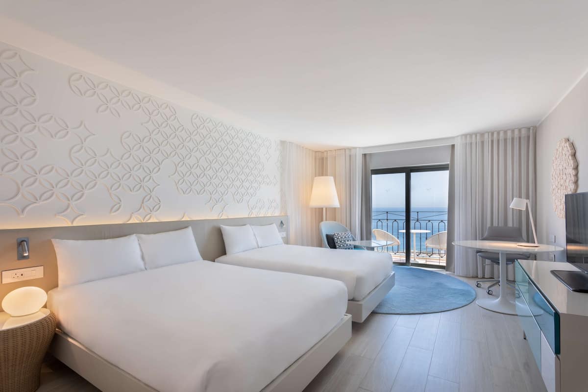 Une chambre d’hôtel avec deux lits, un bureau, une chaise, une télévision et un balcon avec vue.