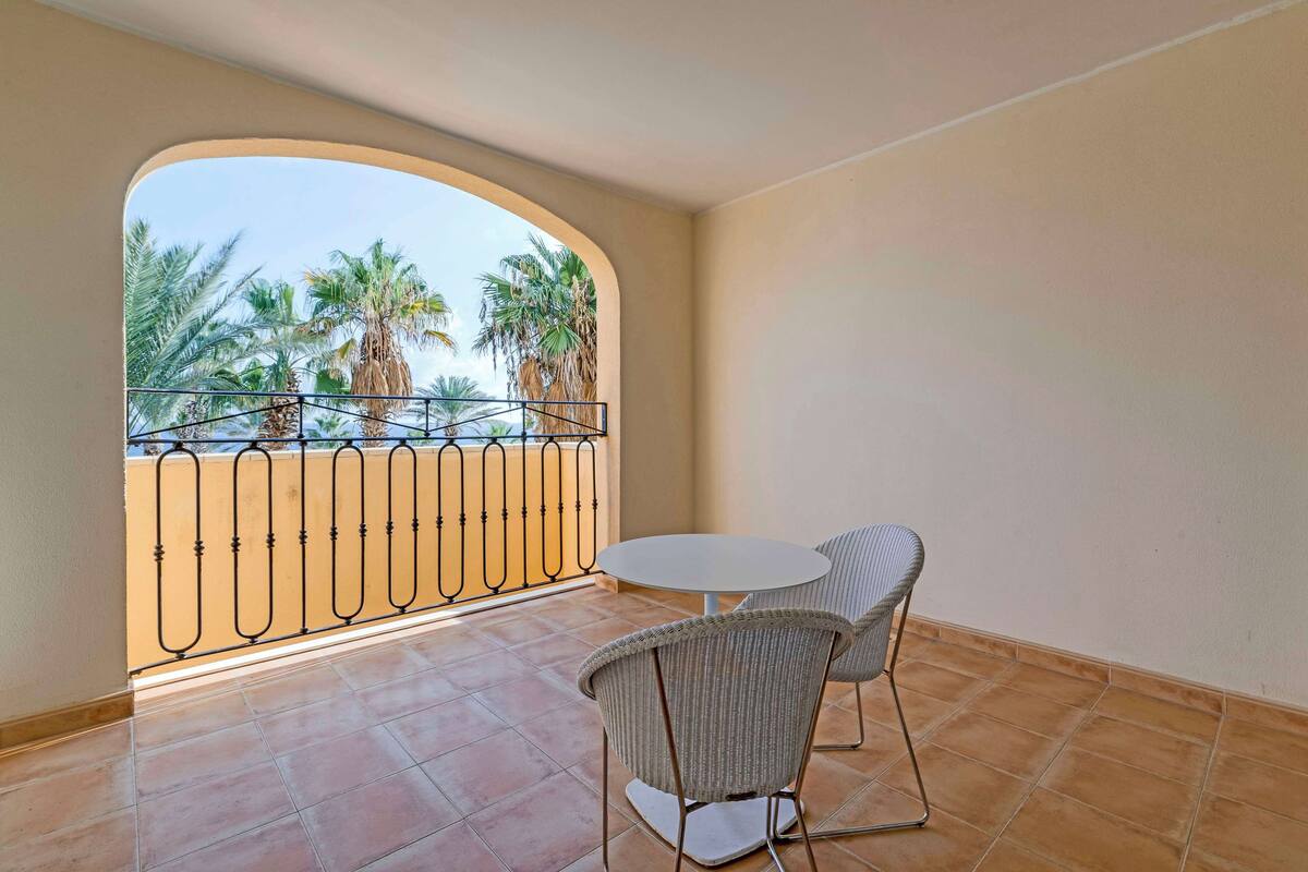 Un balcon donnant sur des palmiers, une table ronde et deux chaises en osier.