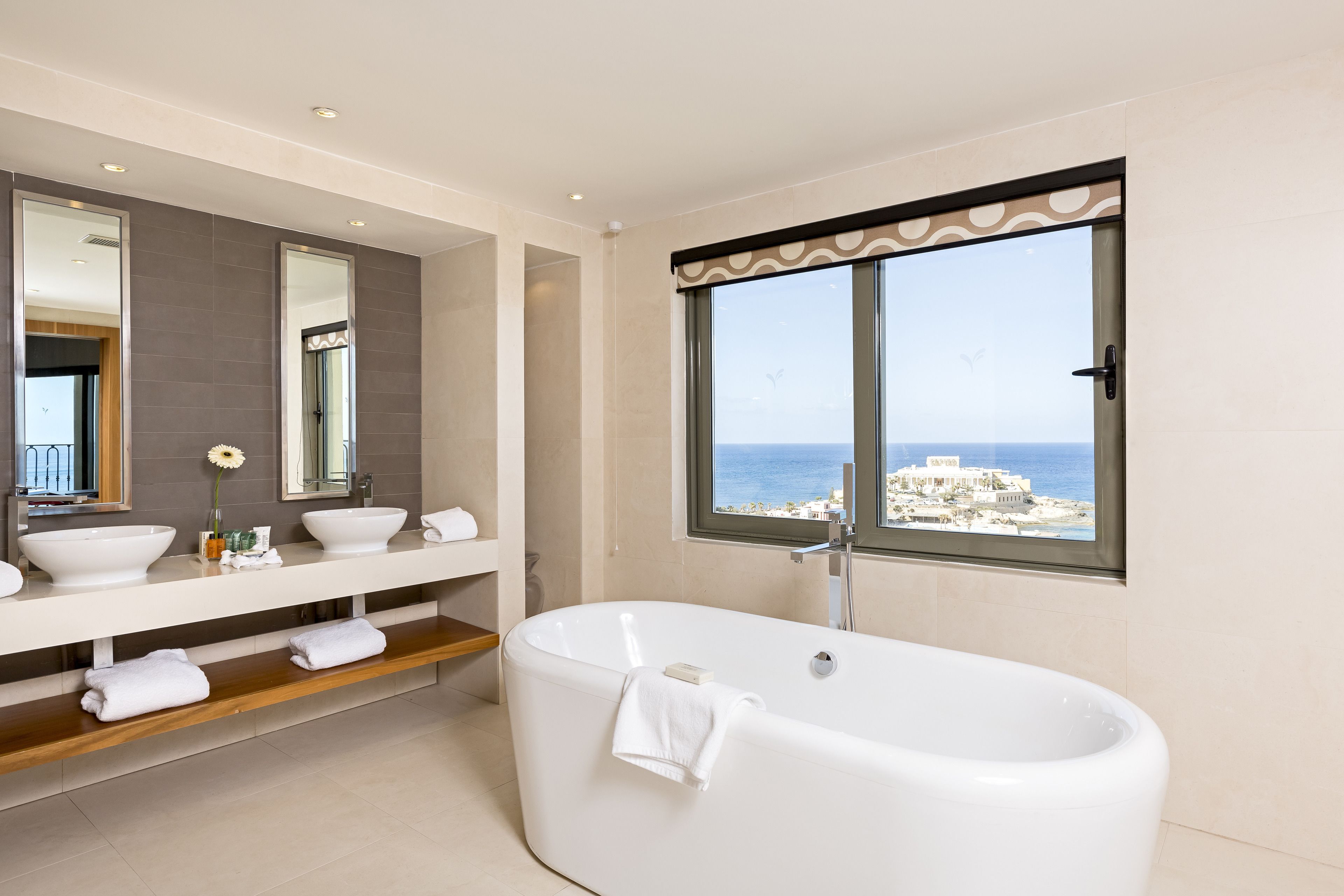 Un baño moderno con una bañera grande, dos lavamanos y un ventanal con vistas al mar.
