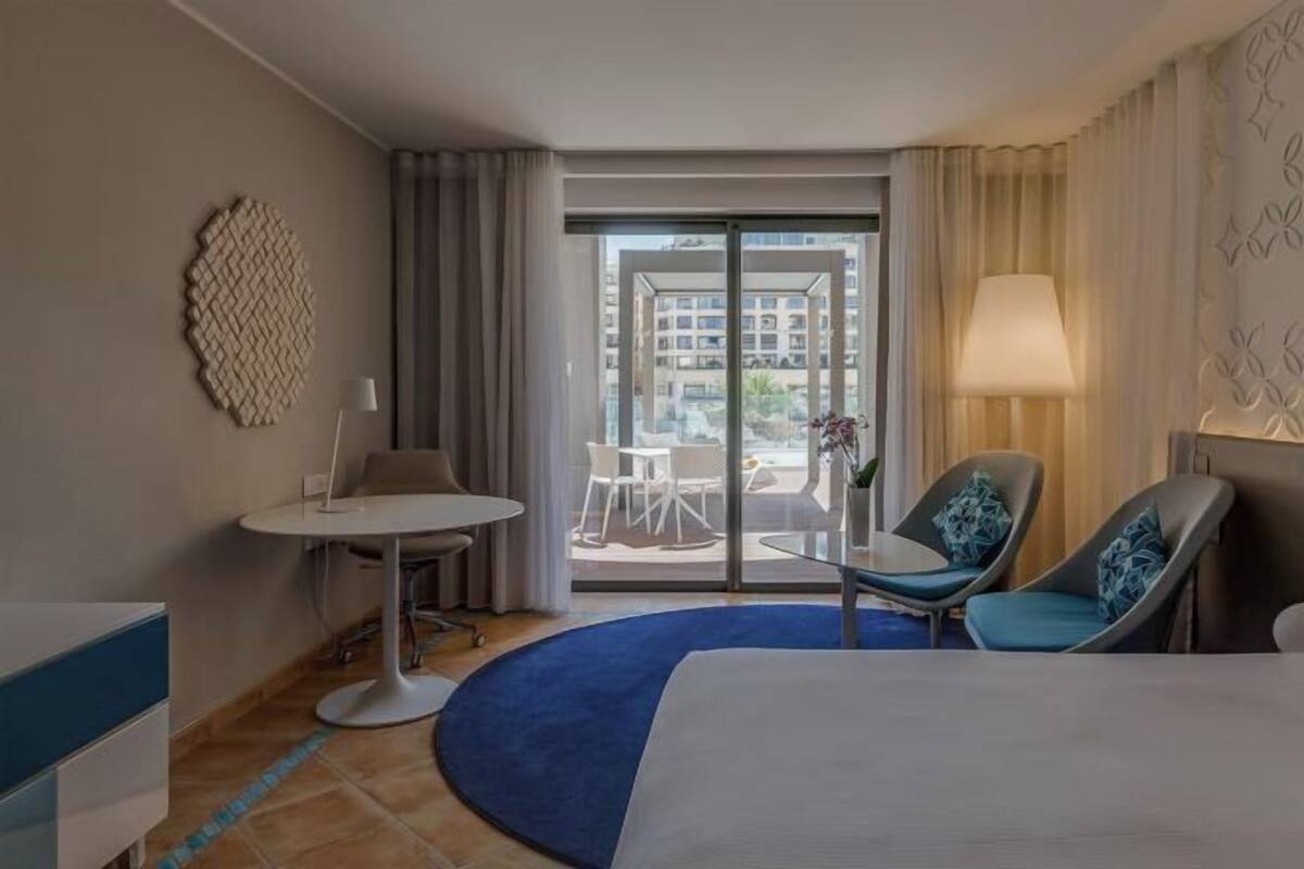 Une chambre d’hôtel avec un lit, une petite table ronde, deux chaises, une lampe et une vue sur l’extérieur.