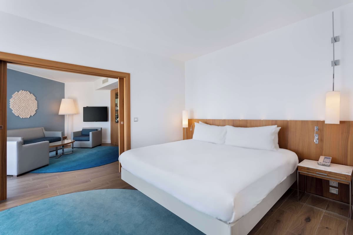 Une chambre d’hôtel moderne avec un grand lit, une table de chevet en bois, un bureau, un canapé et une télévision.