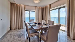 A dining area with a large table set for six, beige curtains, and a view of the ocean. - Hilton Malta (St. Julian's)