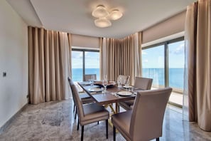 A dining area with a large table set for six, beige curtains, and a view of the ocean. - Hilton Malta (St. Julian's)