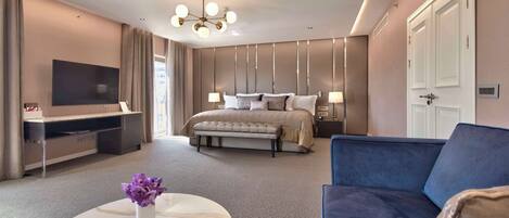 Una habitación de hotel moderna con una cama grande, un televisor de pantalla plana, un sofá y una mesa de centro de mármol con un jarrón de flores.
