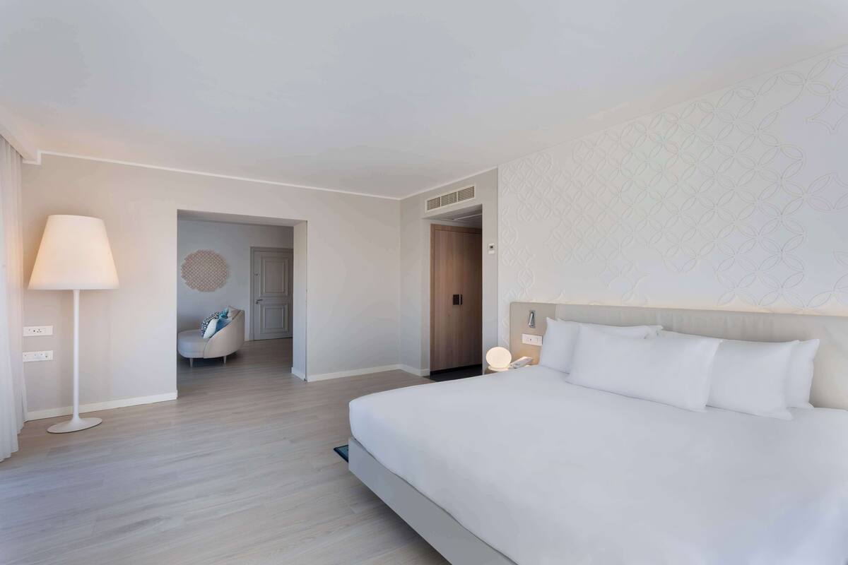Une chambre d’hôtel moderne avec un grand lit, une table de chevet, une lampe et une vue sur le couloir.