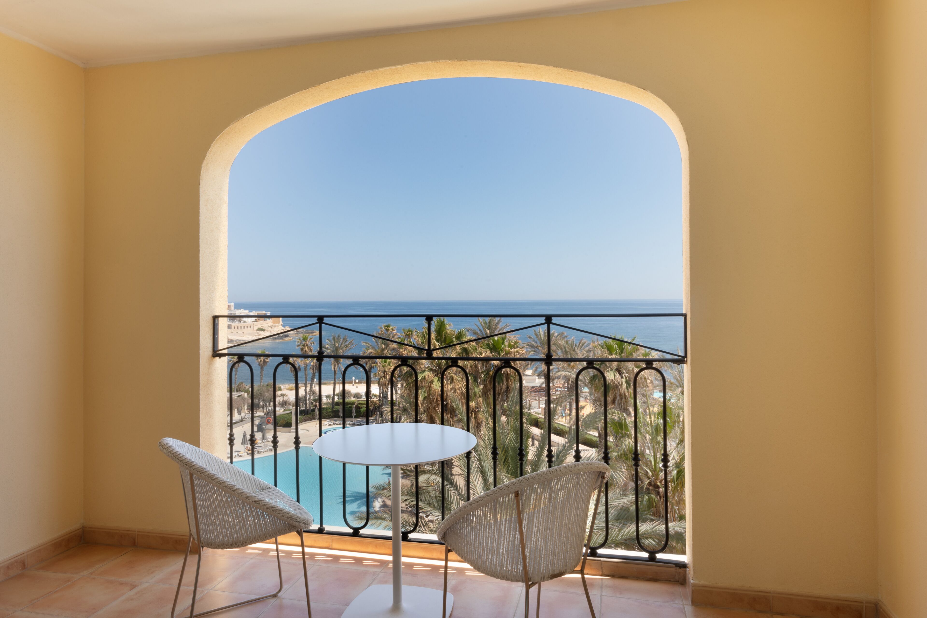A balcony with a view of a pool and palm trees.