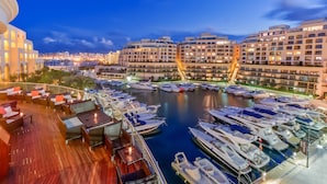 A marina with boats docked, a waterfront promenade with seating, and modern buildings in the background. - Hilton Malta (St. Julian's)
