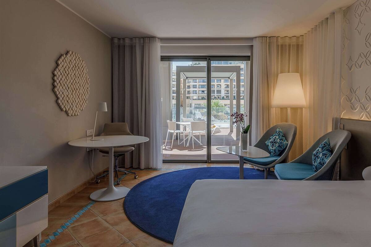 Une chambre d’hôtel avec un lit, un bureau, une chaise et une vue sur le balcon extérieur.