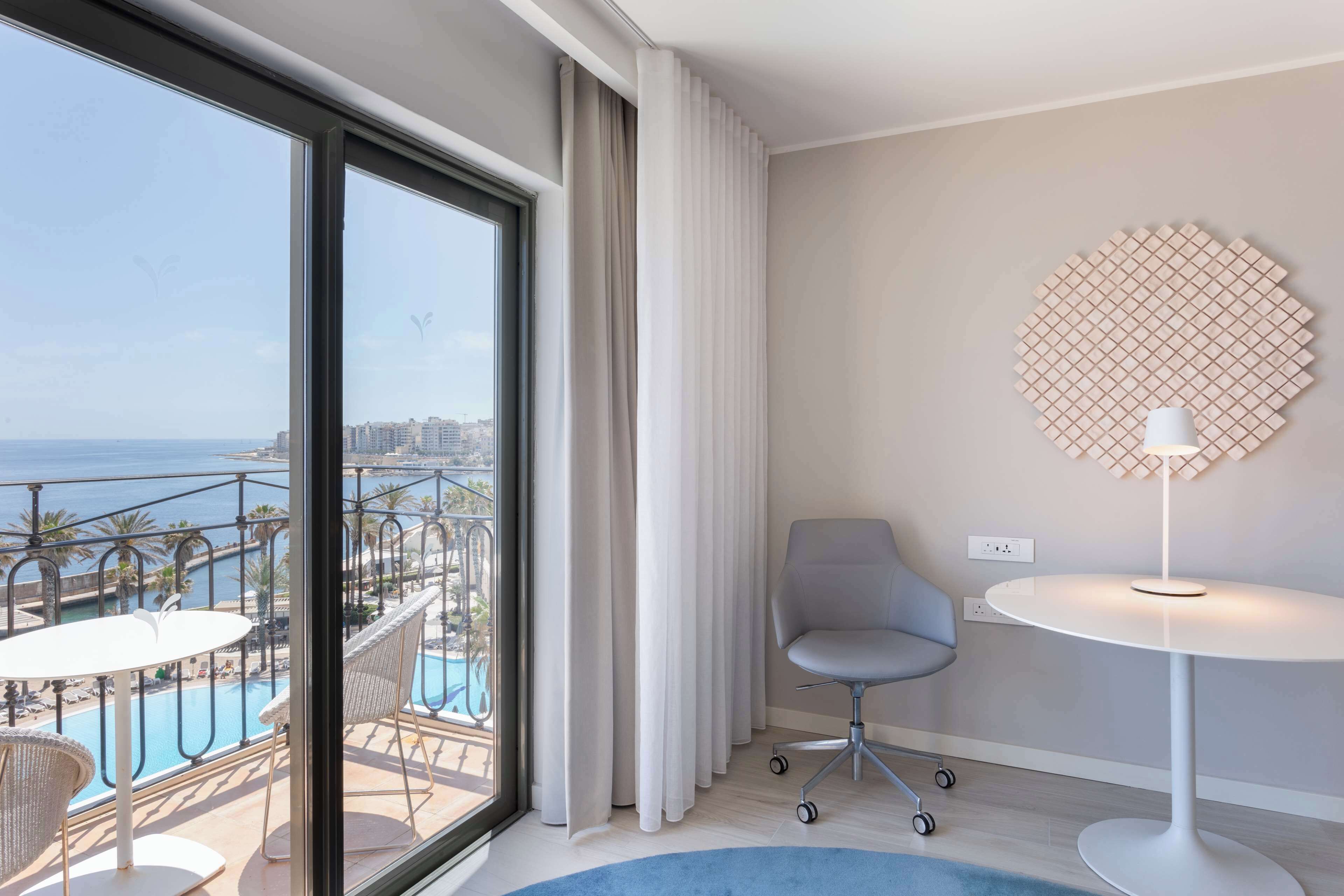 Habitación de hotel con un ventanal que da a una piscina y al paisaje urbano.