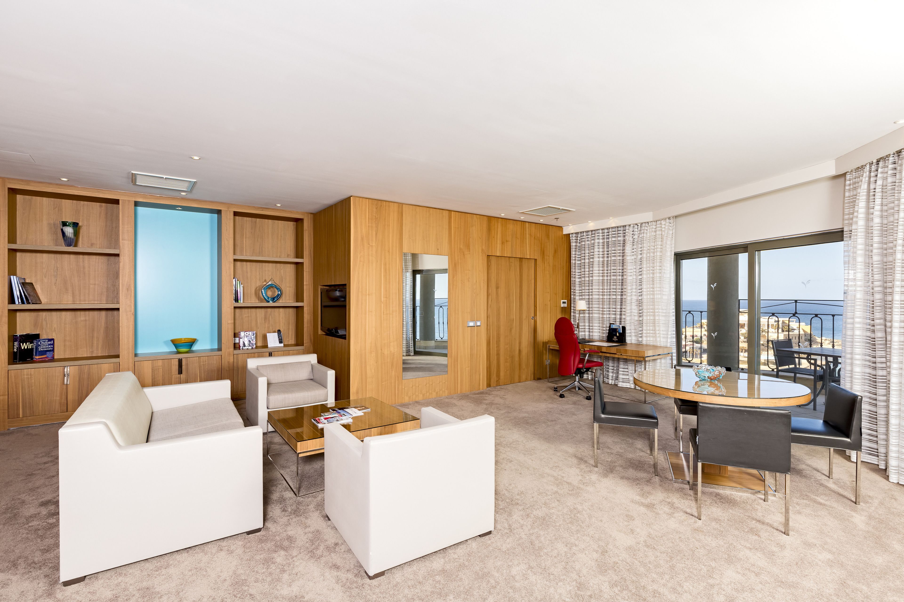 A modern hotel room with a living area, a dining table, and a balcony with a view.