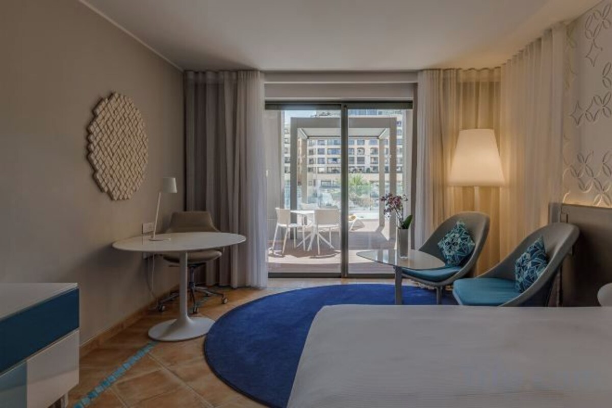 A hotel room with a bed, a desk, a chair, a table, and a view of the outside.