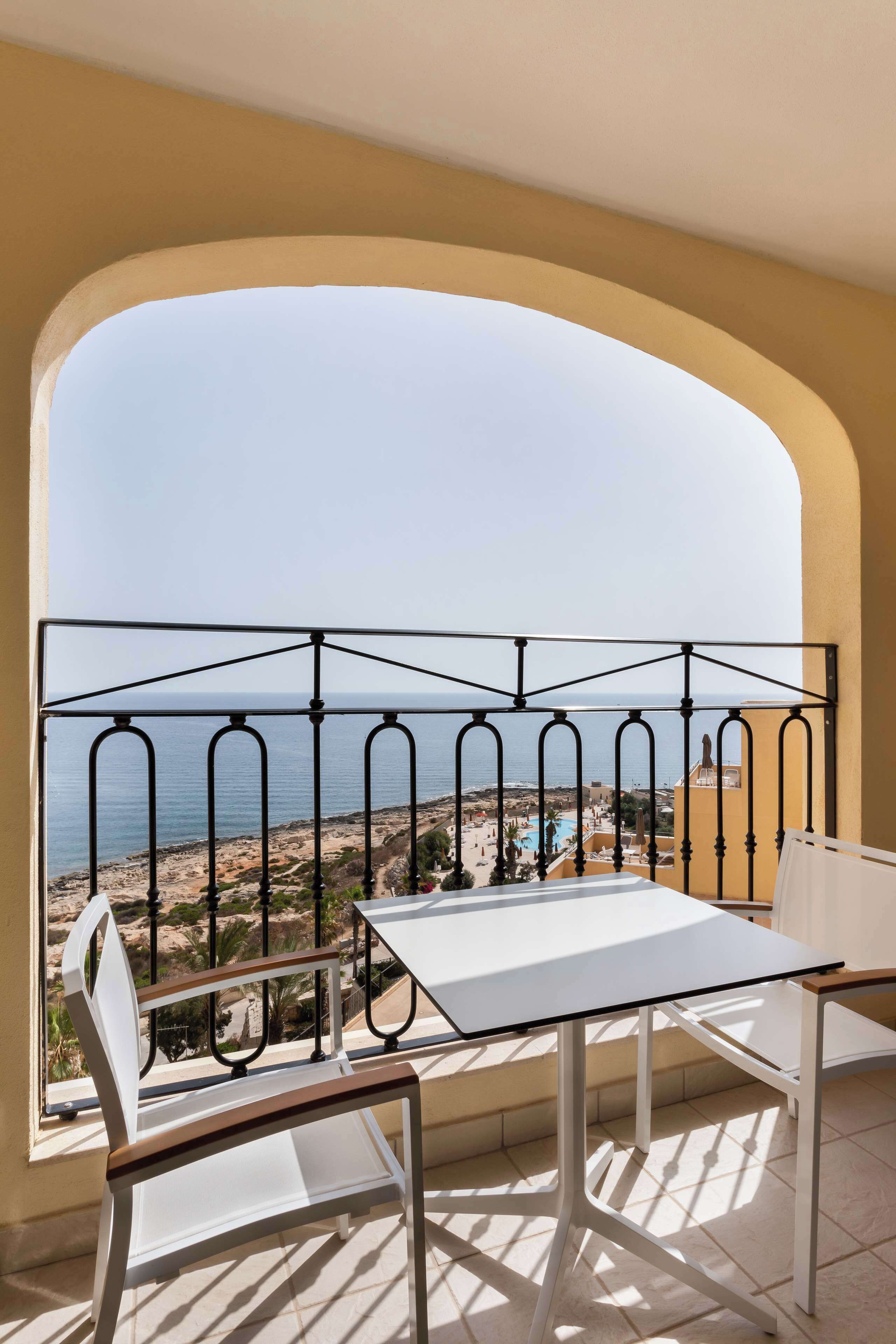 Un balcón con una mesa y silla blancos, baranda de metal y vista al mar y un resort.
