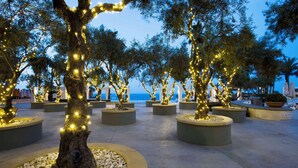 A landscaped area with trees wrapped in lights, surrounded by planters and a paved walkway. - Hilton Malta (St. Julian's)