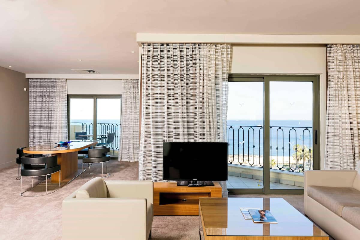 Une chambre d’hôtel moderne dotée d’un balcon, d’une télévision, d’un canapé, d’une table basse et d’un coin repas.